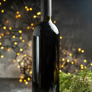 Image représentant une bouteille de vin noir avec des guirlandes lumineuses derrière en décor